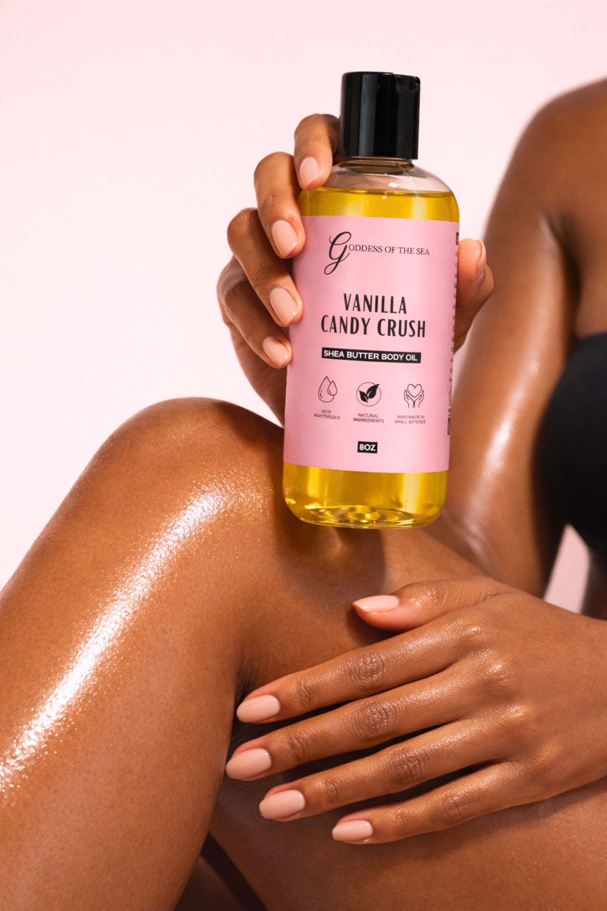 Person applying Vanilla Candy Crush body oil to their skin with a pink background