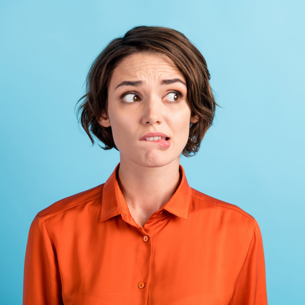 A woman with short brown hair in an orange shirt biting her lip becuase she's worried about a fishy vaginal odor.